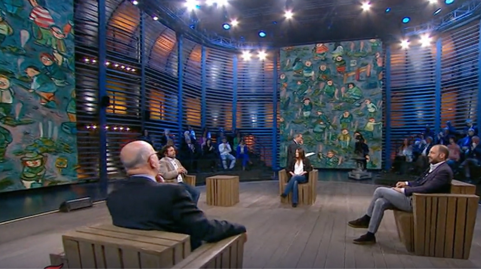 Set televisivo con scenografia ad arena, pareti dipinte d'autore e illuminazione scenica blu