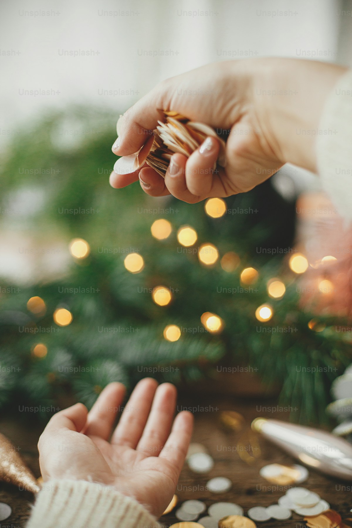 Mani di floral designer che dispongono composizioni floreali su tavolo con bokeh dorato di sfondo
